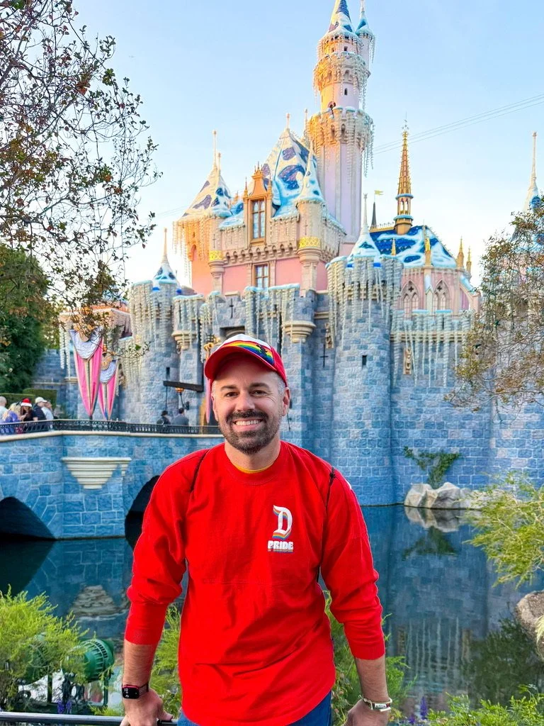 Nick Bryan, founder of Sandpiper Vacations, in a Disney Pride shirt in front of Sleeping Beauty Castle at Disneyland