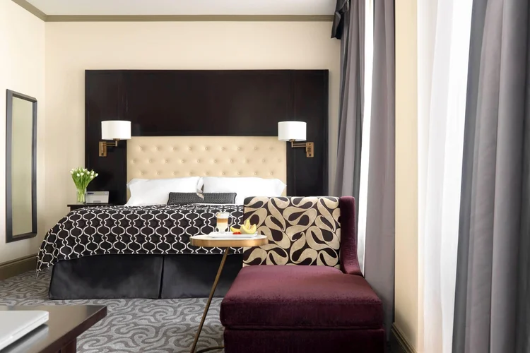 King guest room with a tufted headboard, patterned bedding and a plum chaise lounge