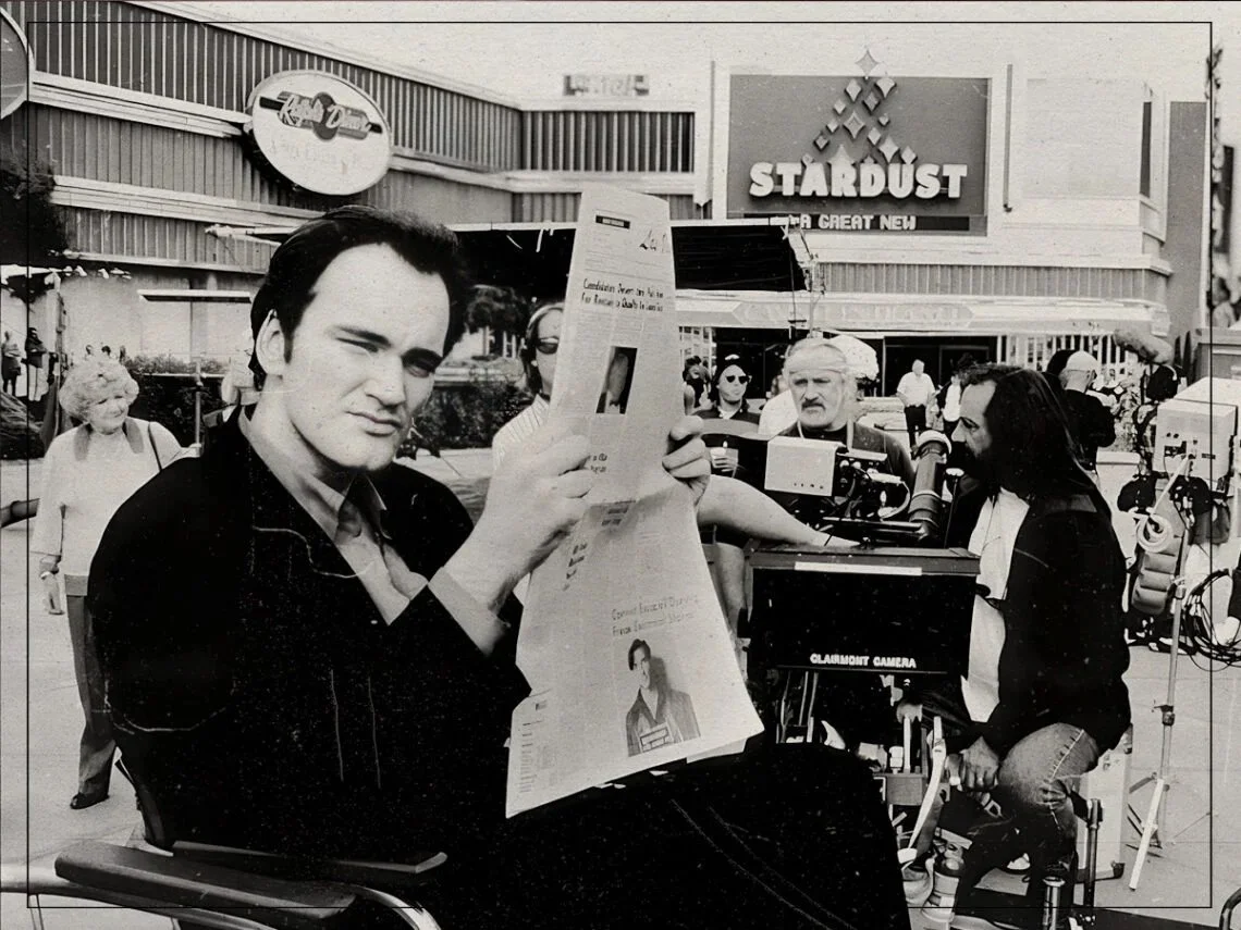 Quentin Tarantino reading a newspaper on a film set, with the Stardust casino marquee in the background