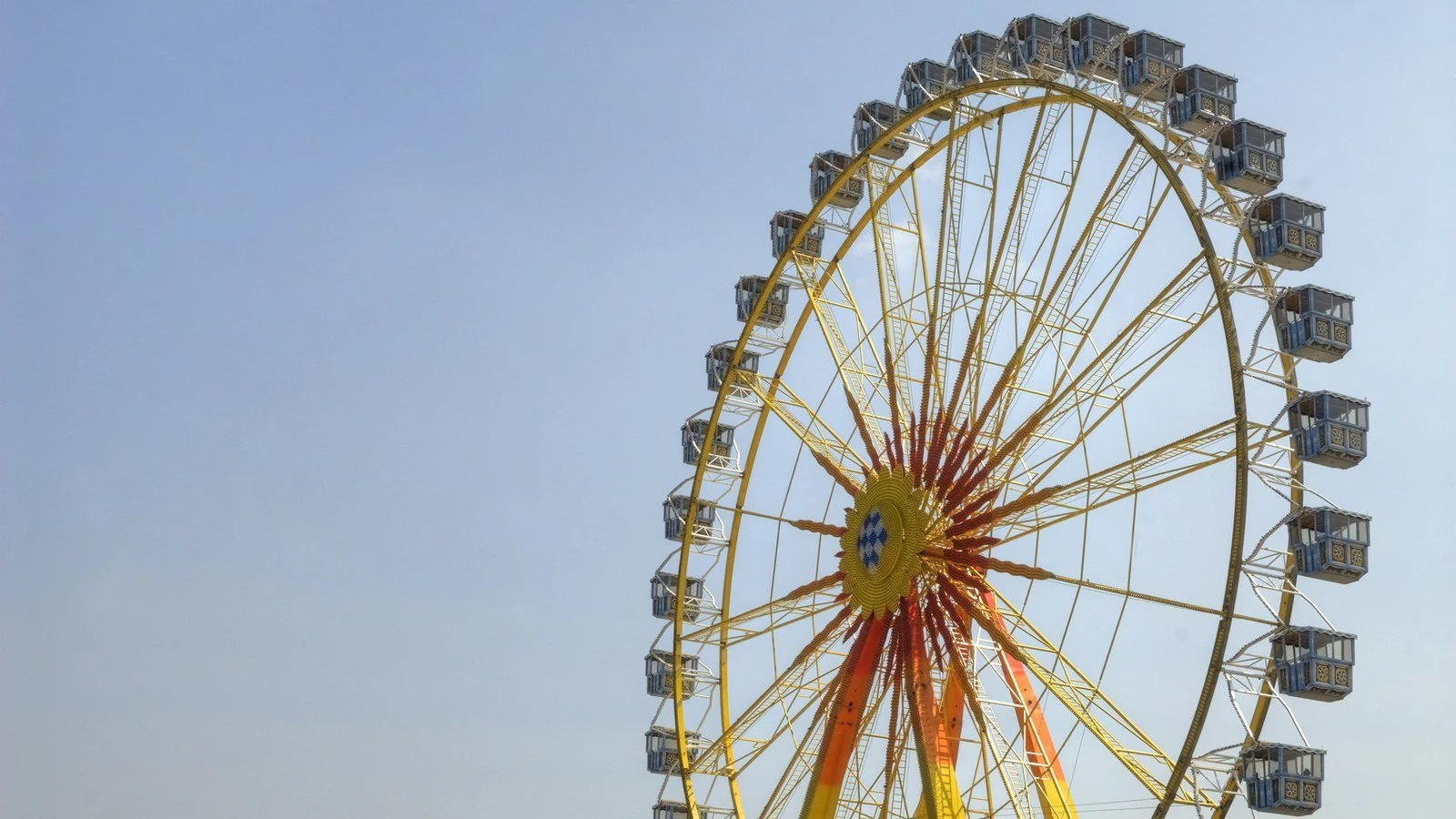 A Ferris wheel against a clear sky, its spoked hub radiating outward like a sunburst.