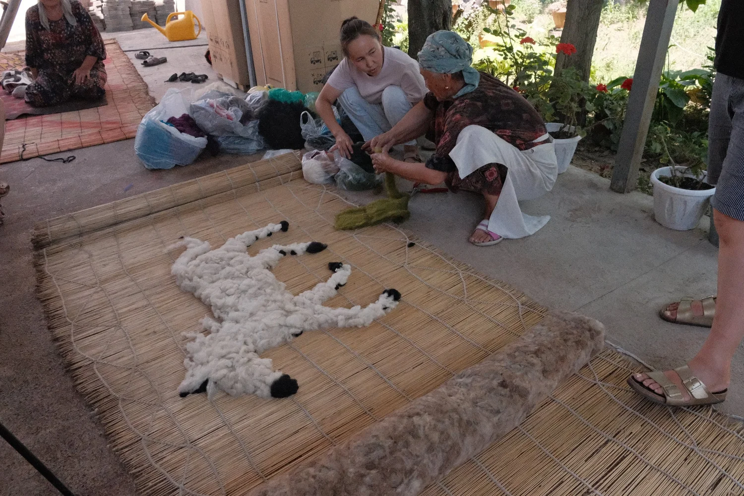 Felt makers laying out wool for a spotted horse design on a reed mat