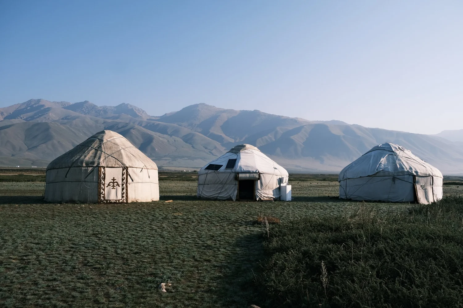 Three white yurts on the open steppe in early morning light
