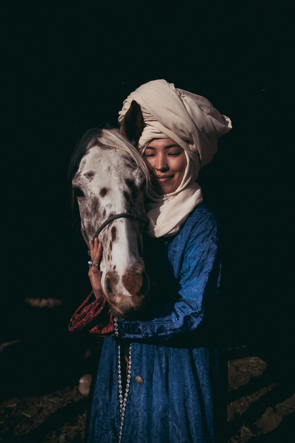 Une femme coiffée d'un turban blanc se tient debout avec un cheval Chaar tacheté