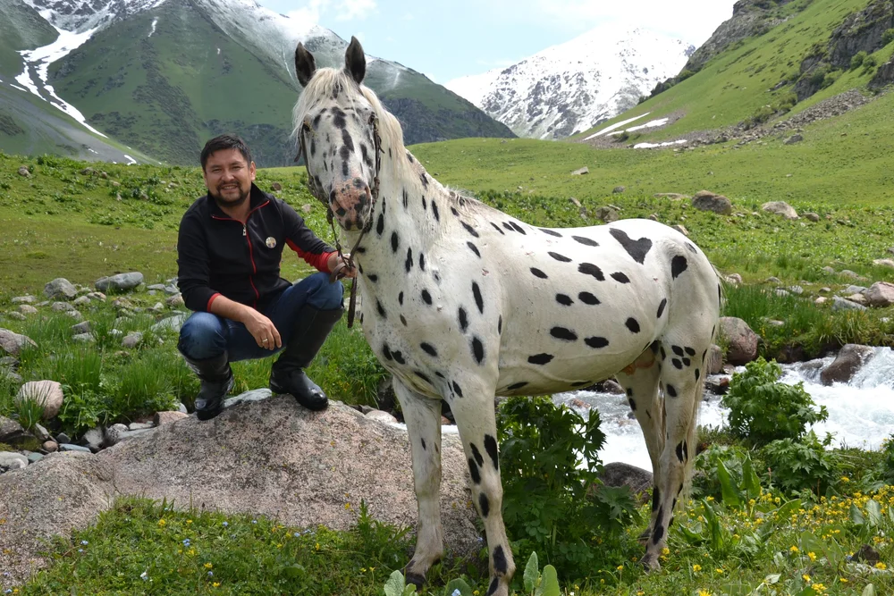 Munarbek Kuldanbaev beside a spotted stallion by a river