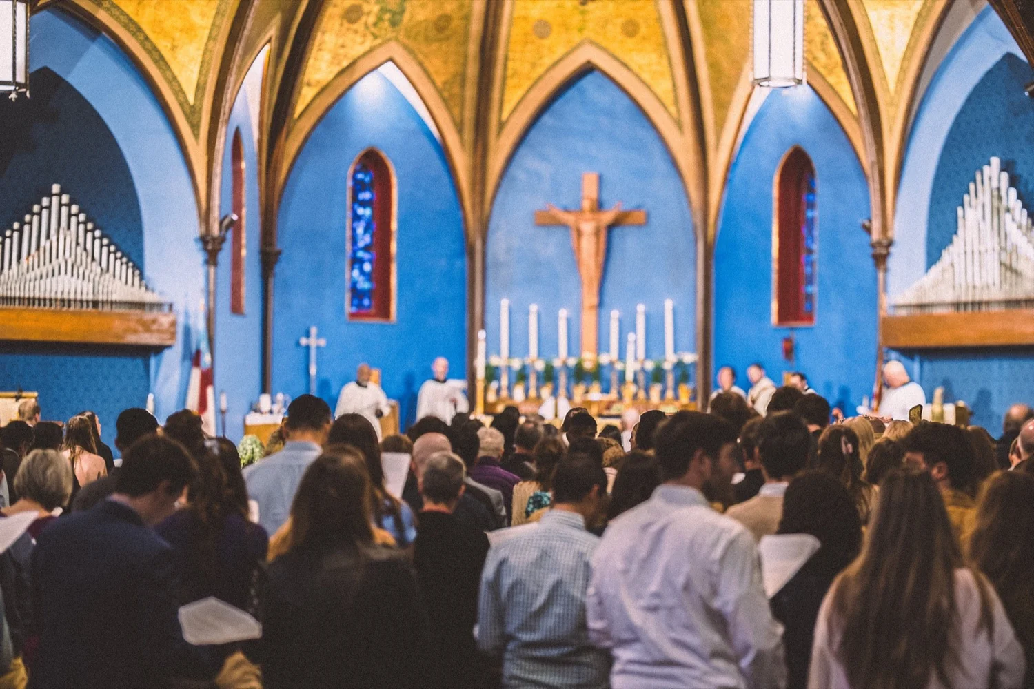 A full church standing in worship at St. John's, under the gold ceiling and blue walls