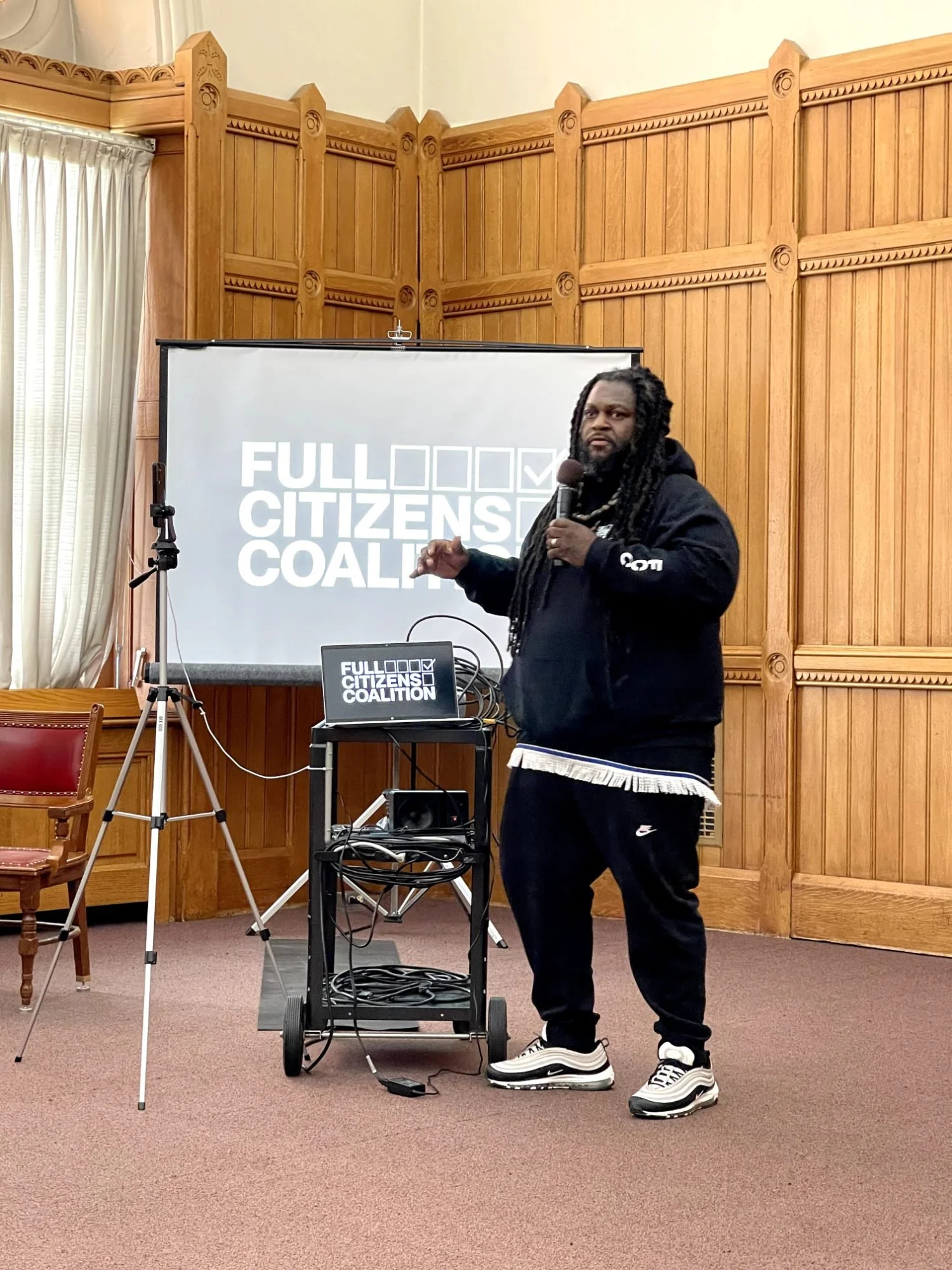 An organizer presents a workshop in a wood-paneled hall
