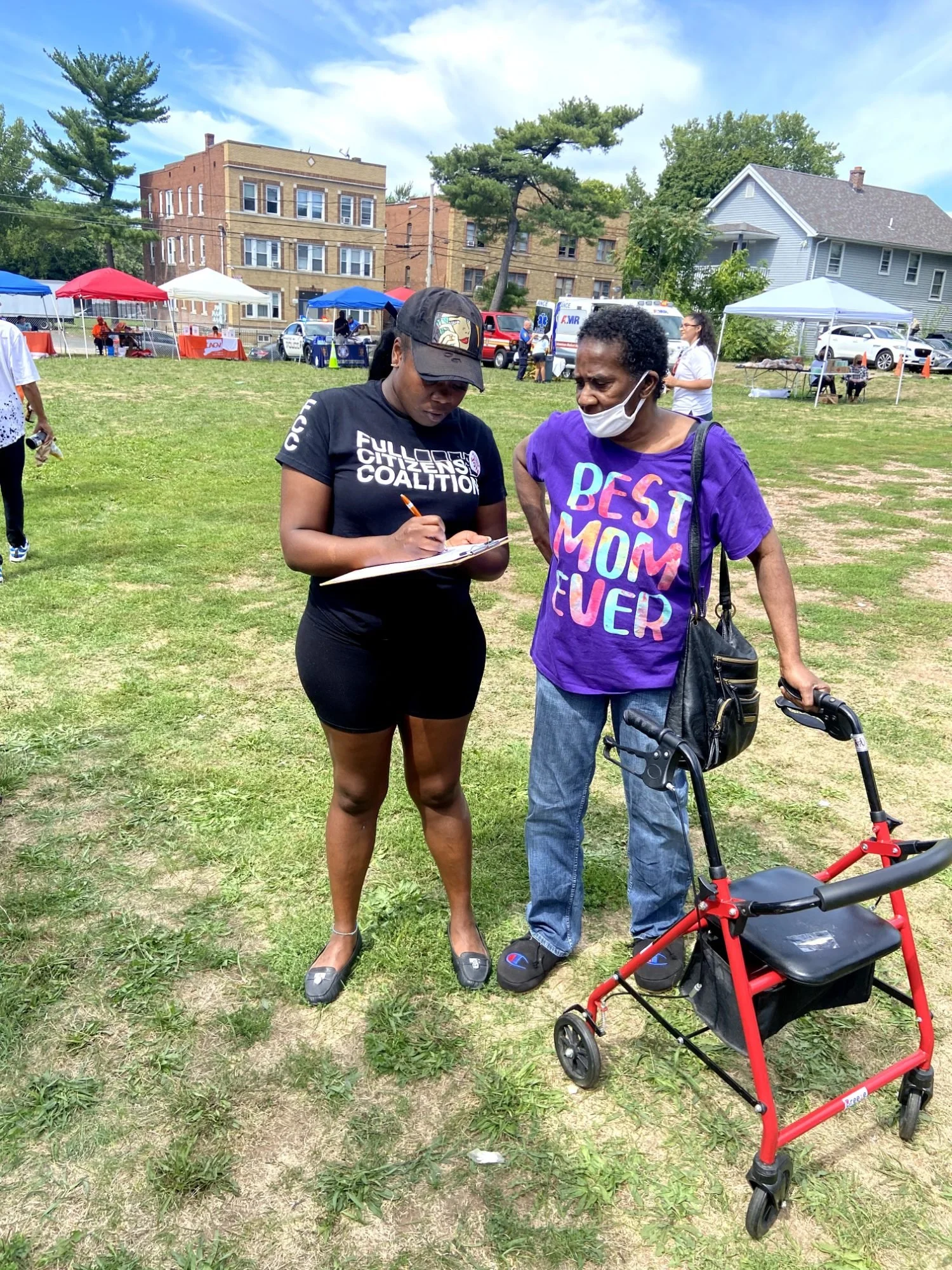 Two women registering voters with a clipboard at a park event
