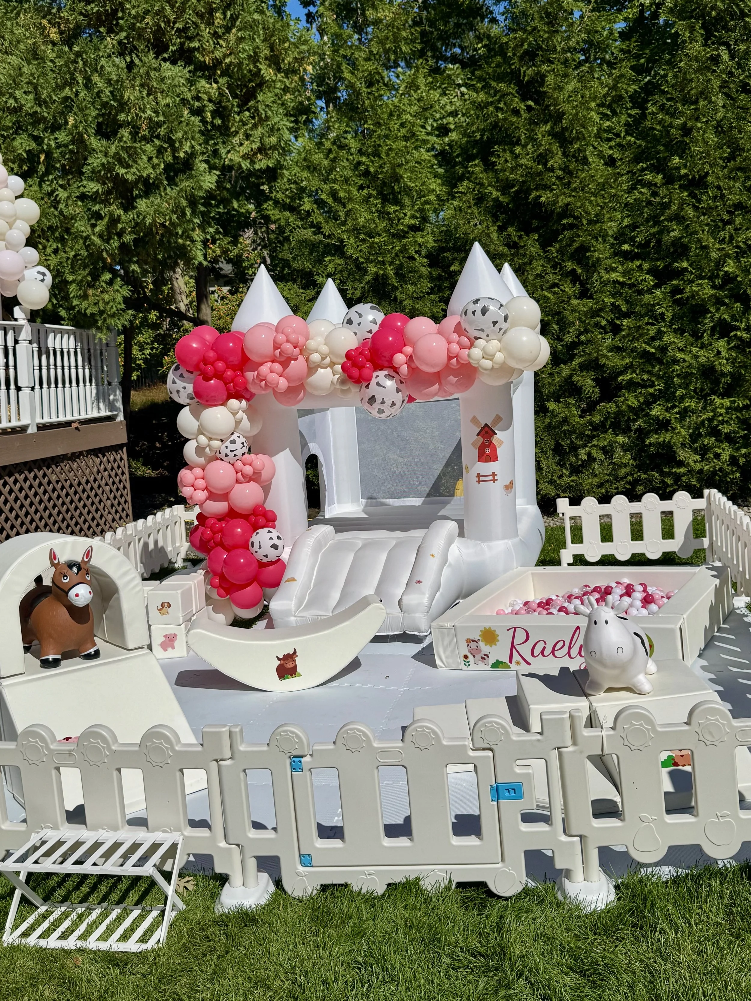 Styled Toddler Soft Play with pink and cow print balloon garland, white bounce house and personalized ball pit