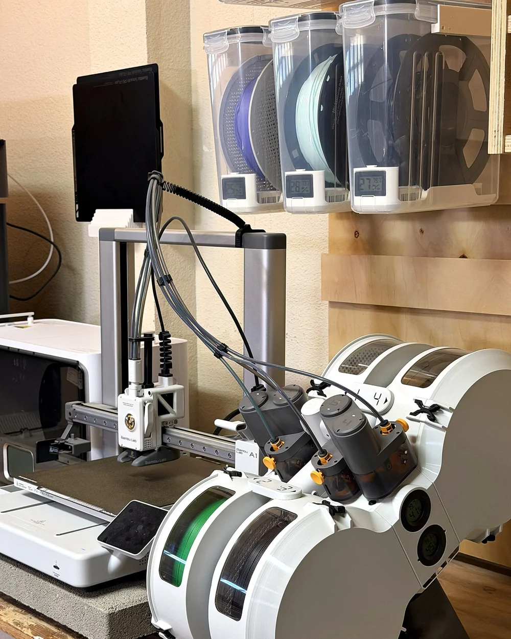 A 3D printer with a four-spool filament feeder and a wall of filament bins
