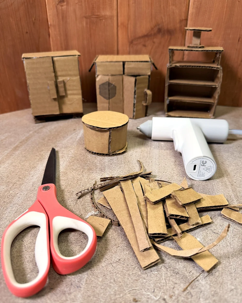 Cardboard prototypes of small furniture with scissors, a glue gun, and cardboard scraps
