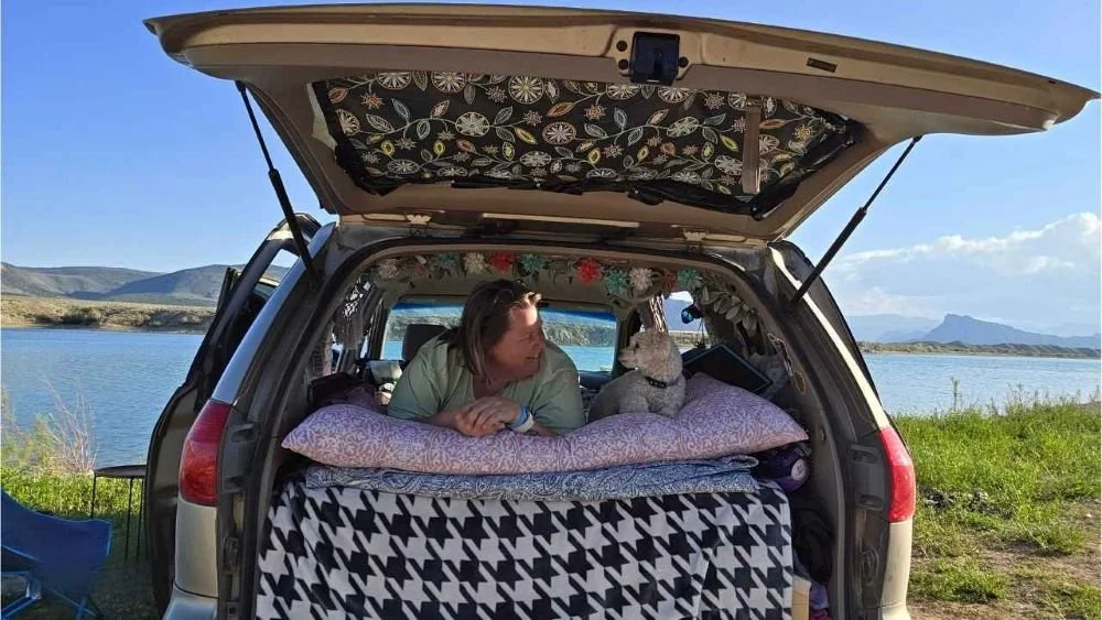 Catina and her dog Henry relaxing on the Roadloft bed platform with the hatch open at a lakeside campsite