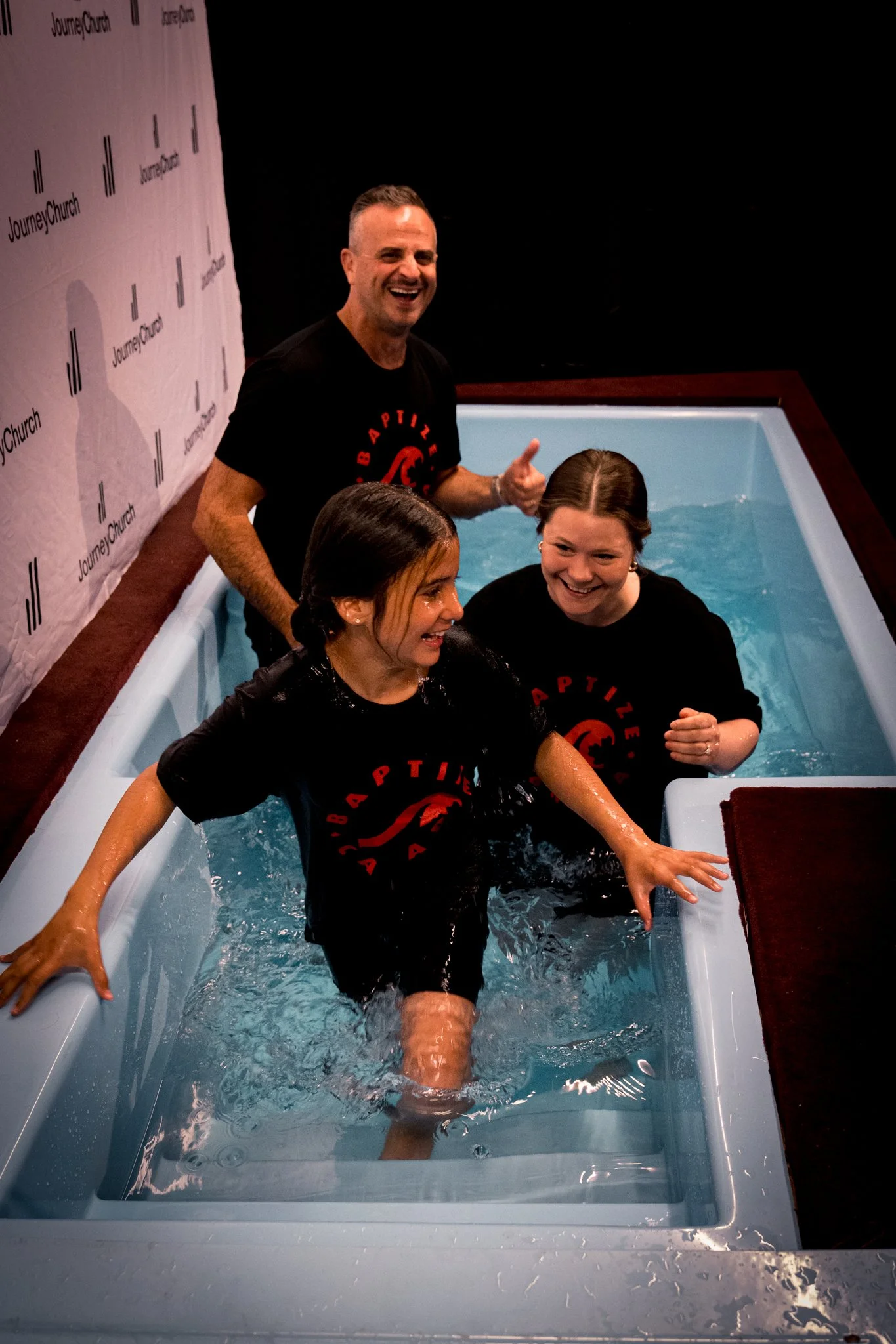 Two young women celebrate in the baptism tank at Journey Church
