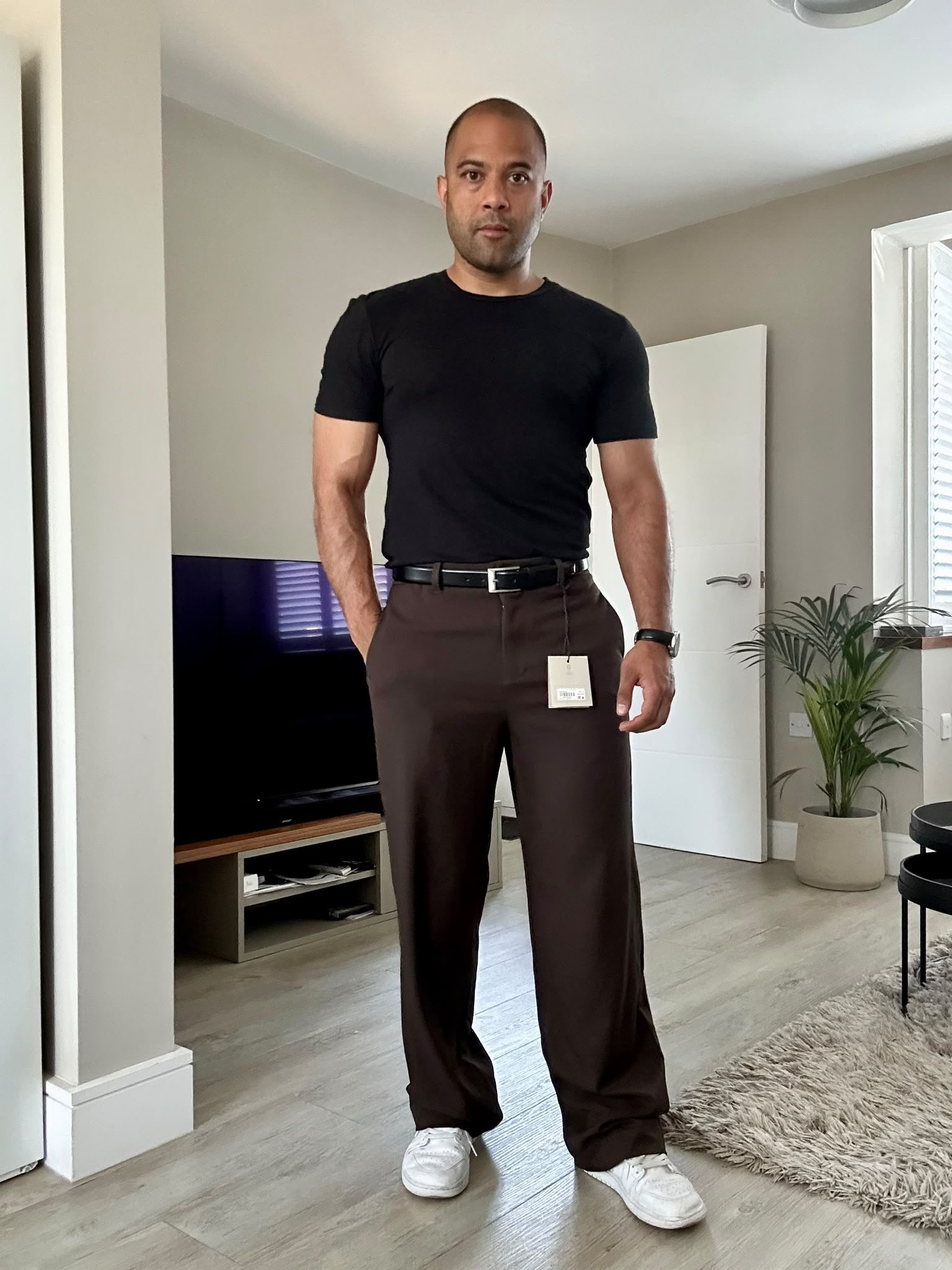 After styling: client wearing a black shirt tucked into brown trousers with a belt and white sneakers.