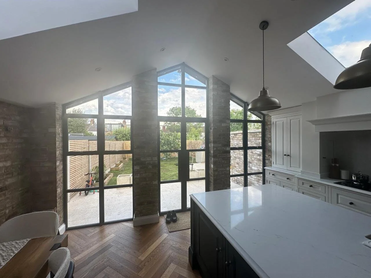 Open-plan kitchen extension with full-height glazing, herringbone flooring, and exposed brick, E4 London. Designed by Bashkal.