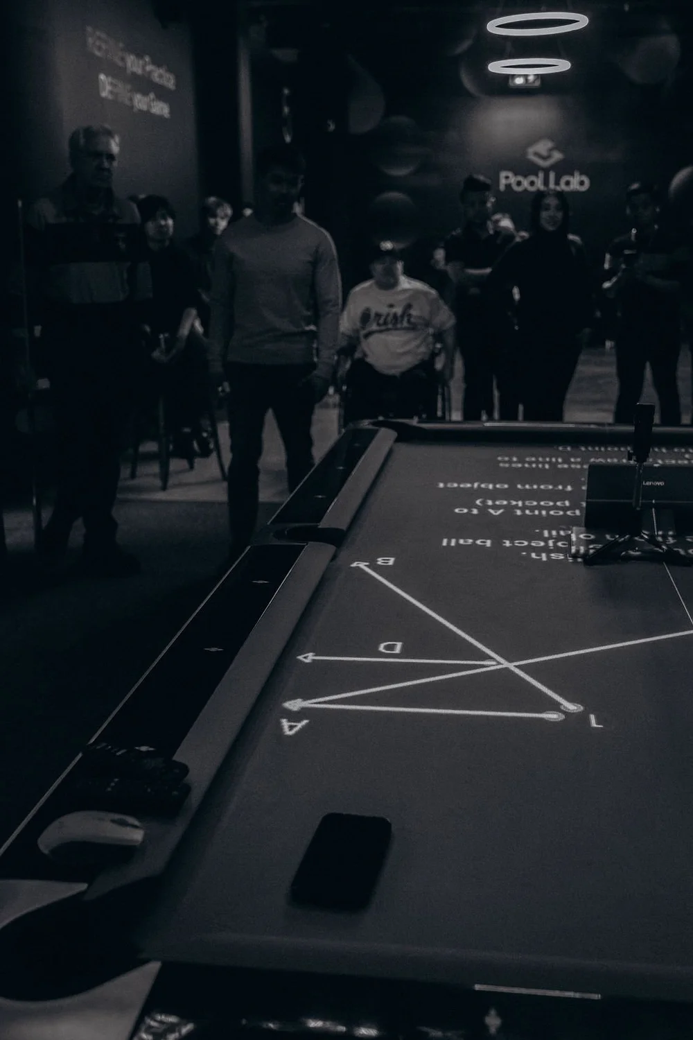 Billiards training drill projected onto the Rasson 9ft Arena table at Pool Lab, with players watching a drill projector session