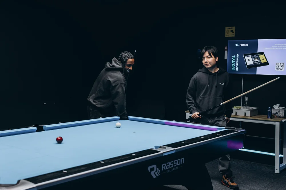 Two players at a Rasson 9ft pool table with Simonis 860HR tournament blue cloth and the Pool Lab digital scoreboard in a private room