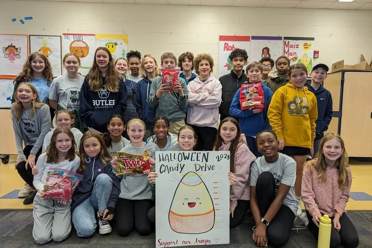 Students holding candy and a Halloween candy drive sign