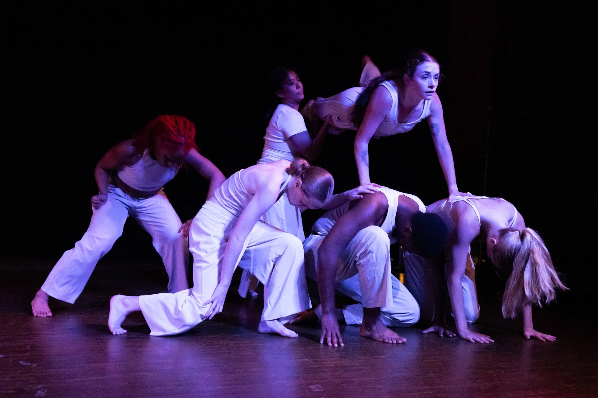 Dancers in low light form a structure by lifting each other up
