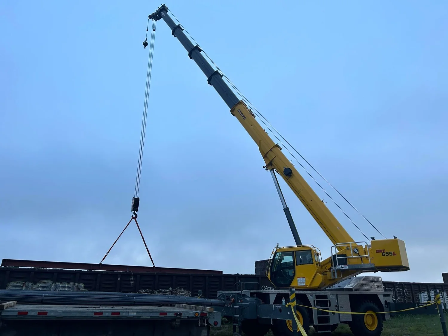 Rough-terrain crane rigging steel beside a rail car