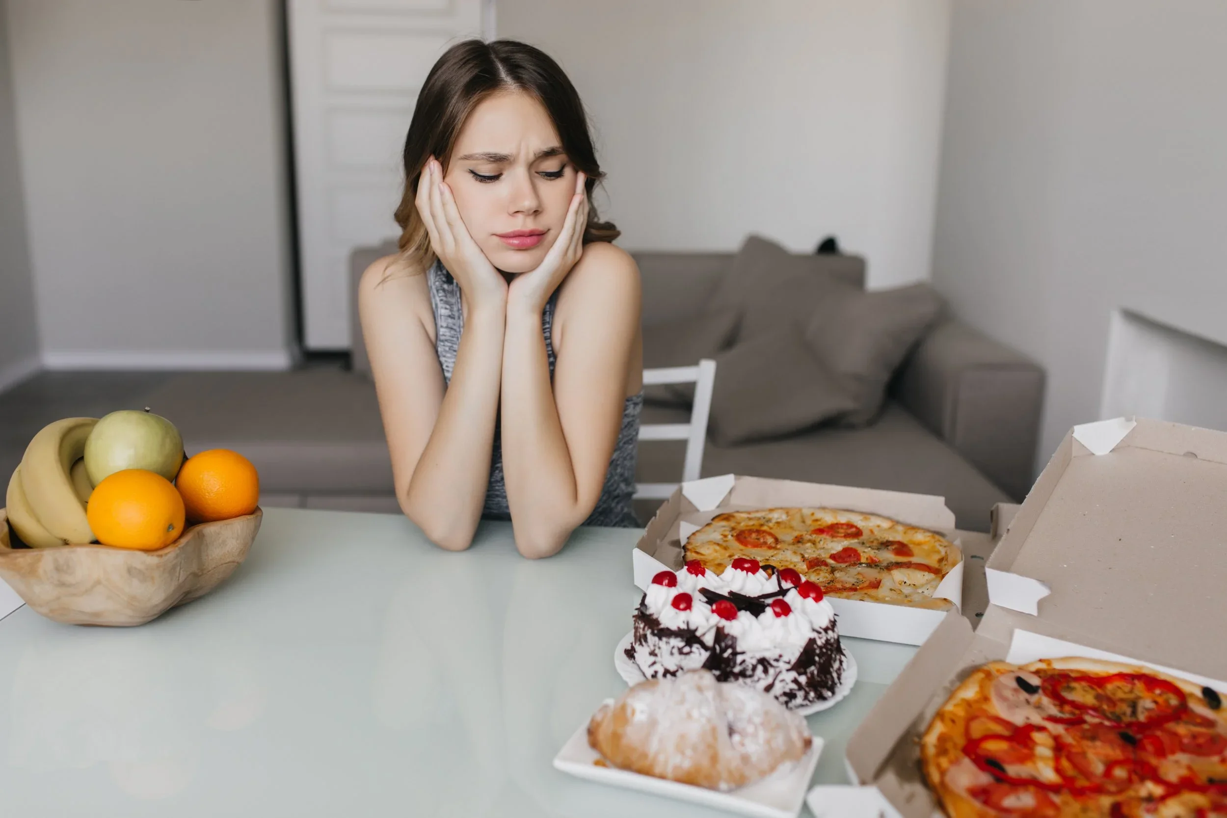 Woman looking distressed while sitting at a table with several foods