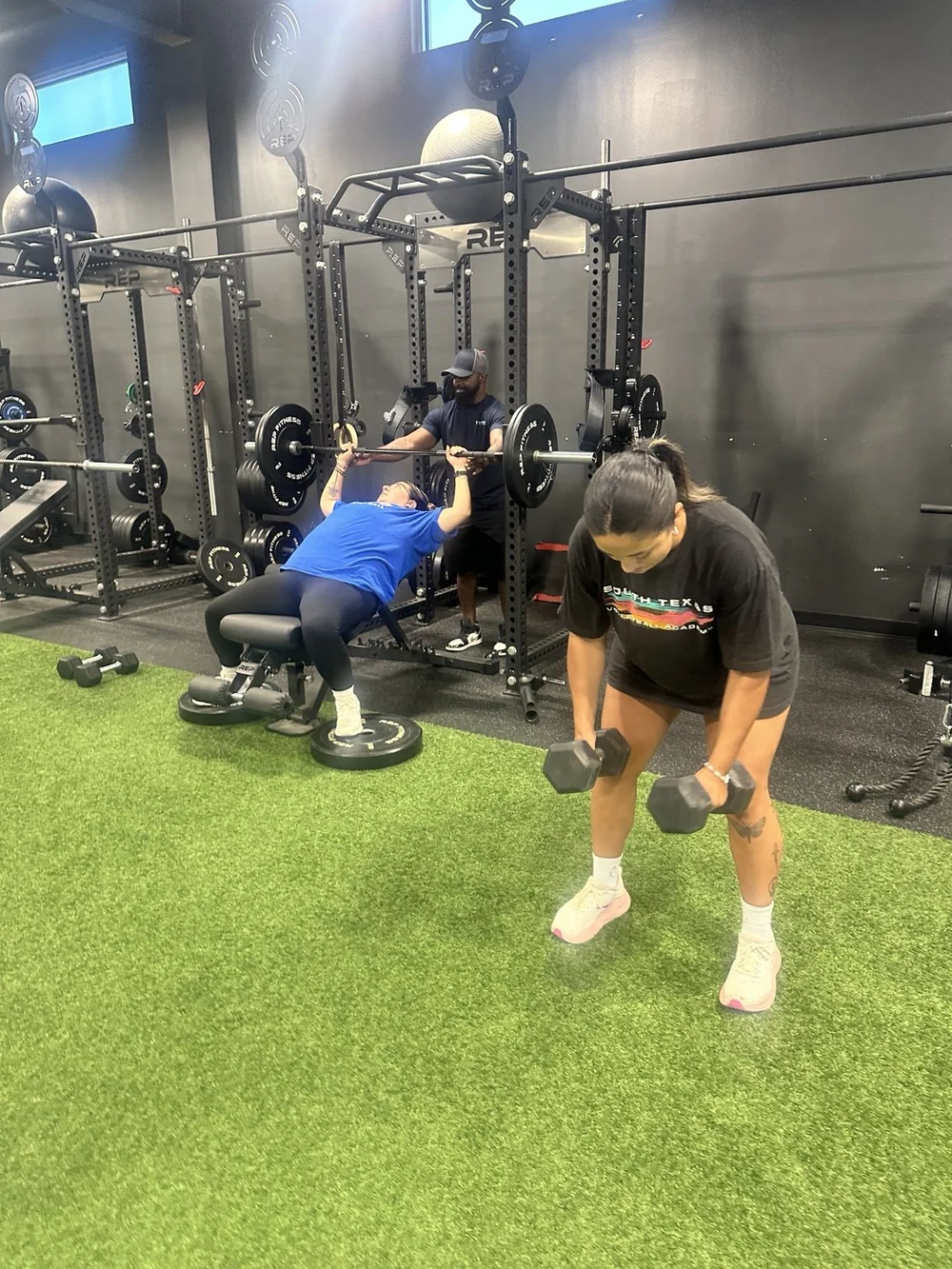 Coach supervising an incline bench press while another member performs dumbbell rows