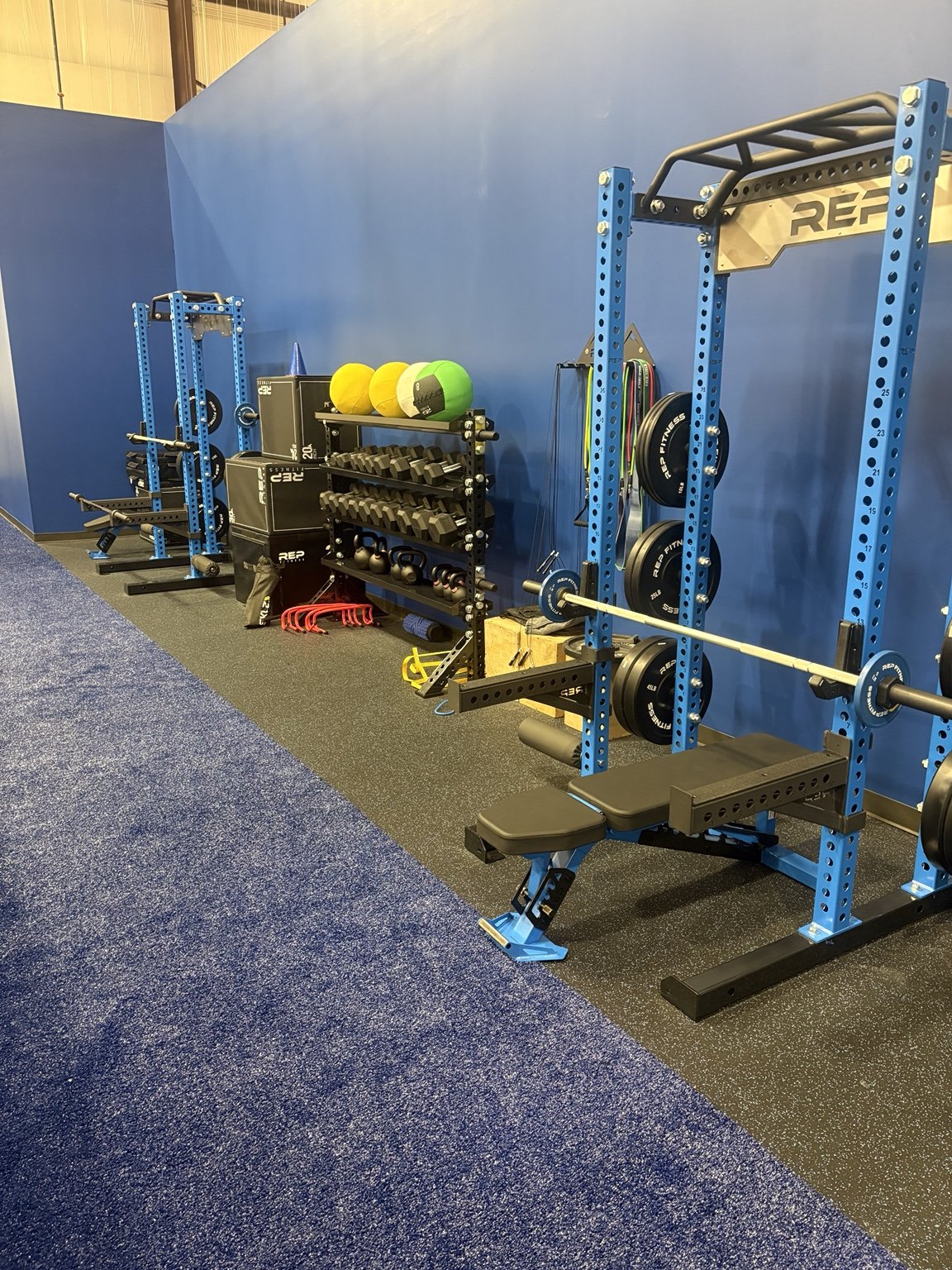 Blue strength racks, free weights, and training lane at MaxxFIT Katy