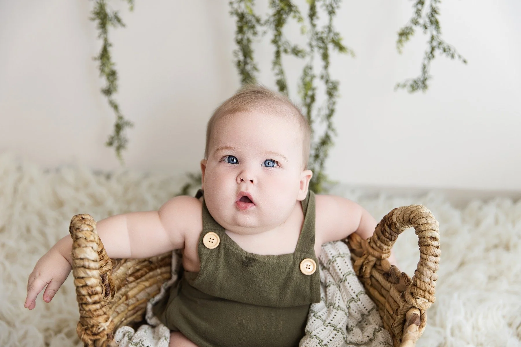 Paxton wearing a green romper in a wicker basket