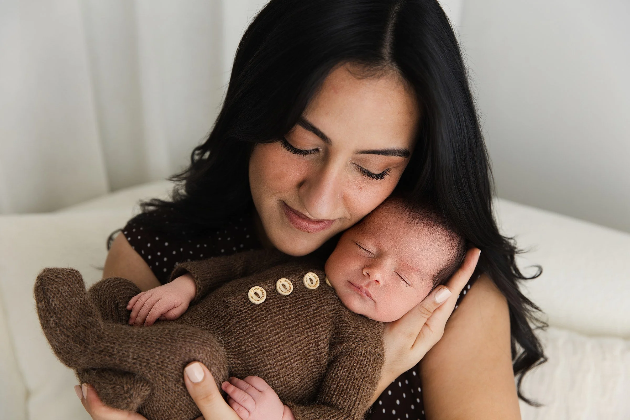 A mother cuddling her sleeping newborn against her cheek.