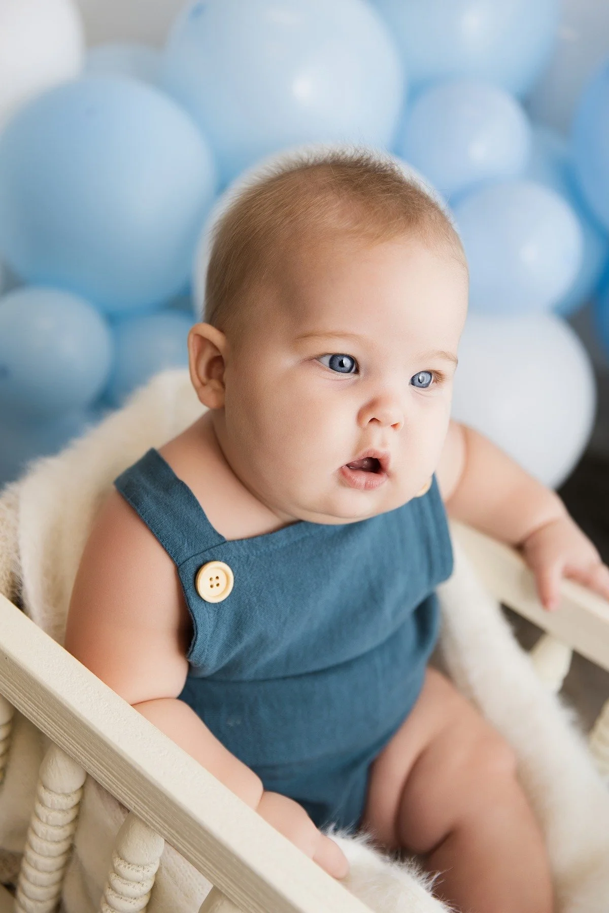 Close-up of Paxton in a blue romper with soft blue balloons behind him