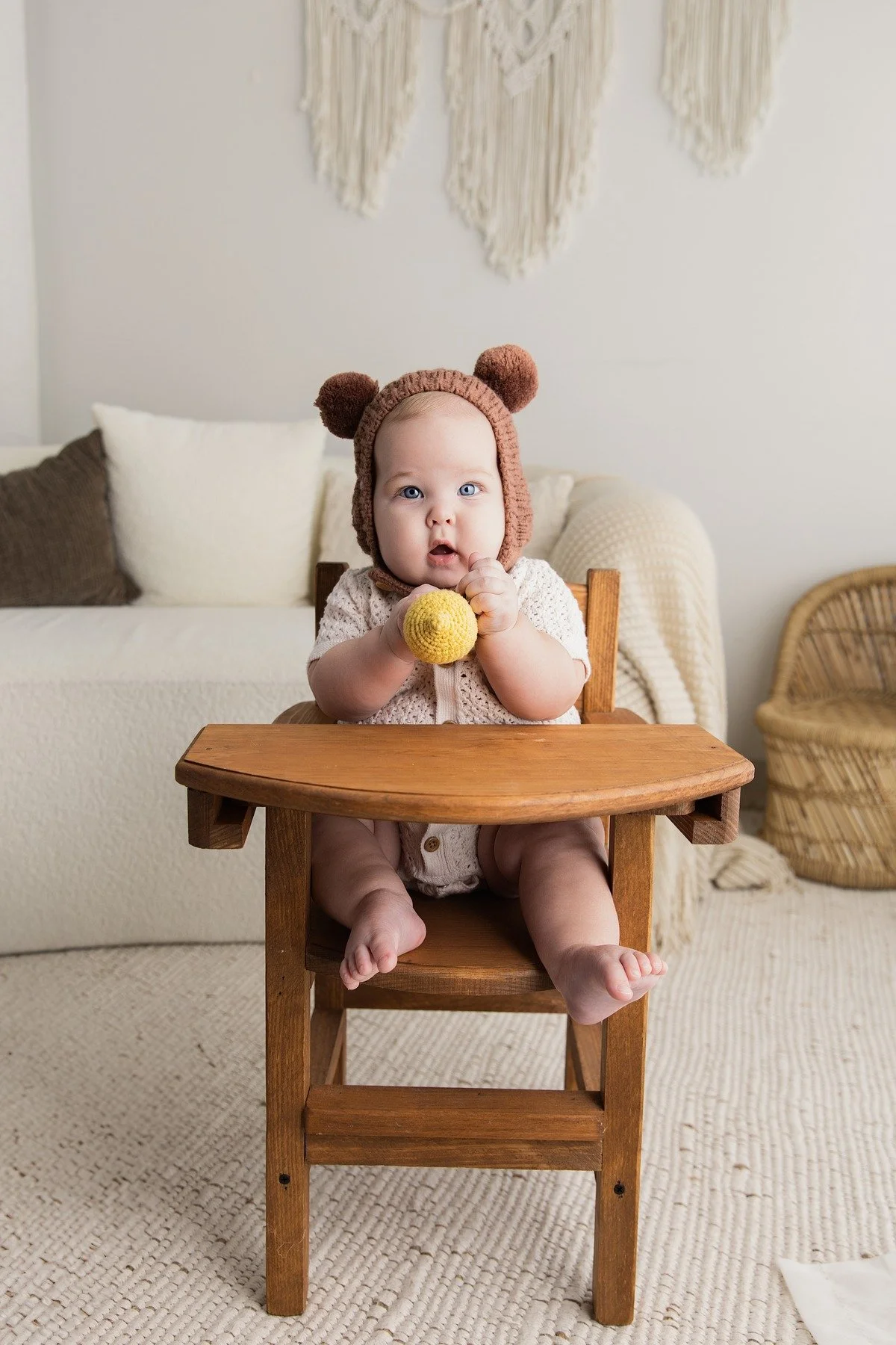 Paxton sitting in a wooden high chair wearing a bear bonnet