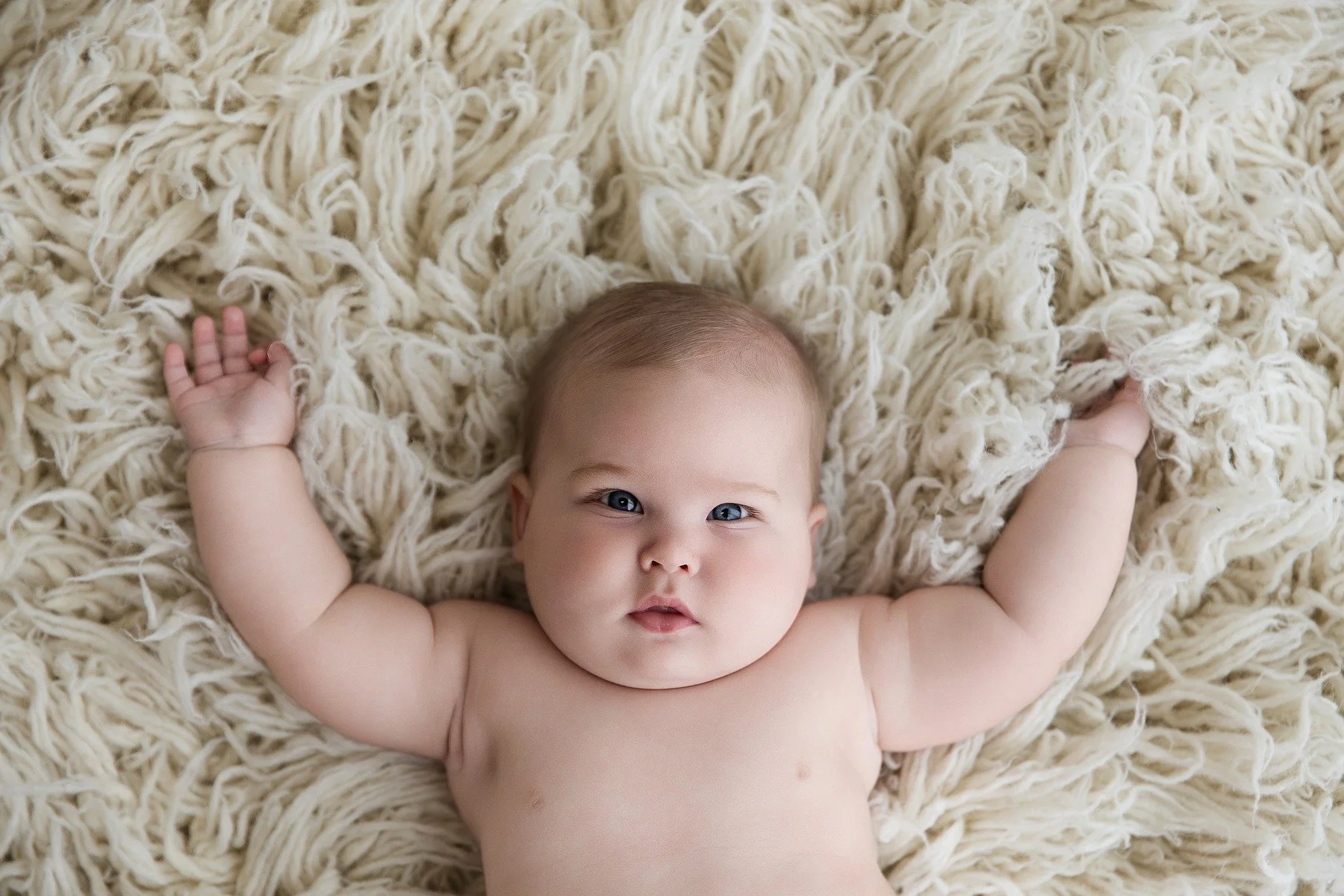 Paxton lying on a soft cream blanket with his arms raised