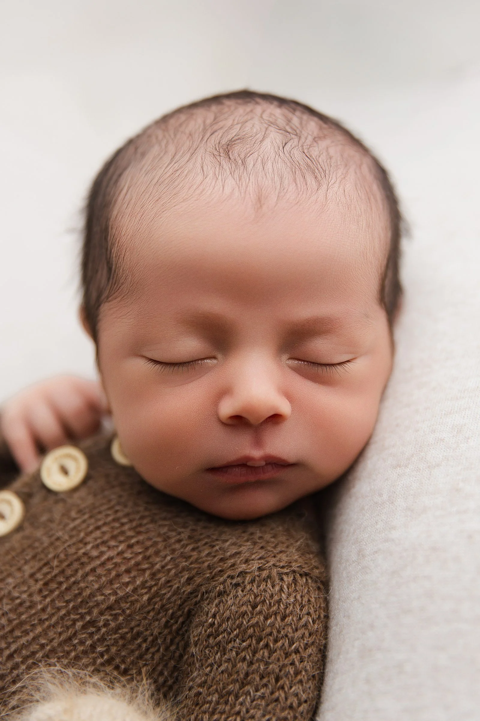 Close-up of a sleeping newborn in a soft brown knitted outfit.