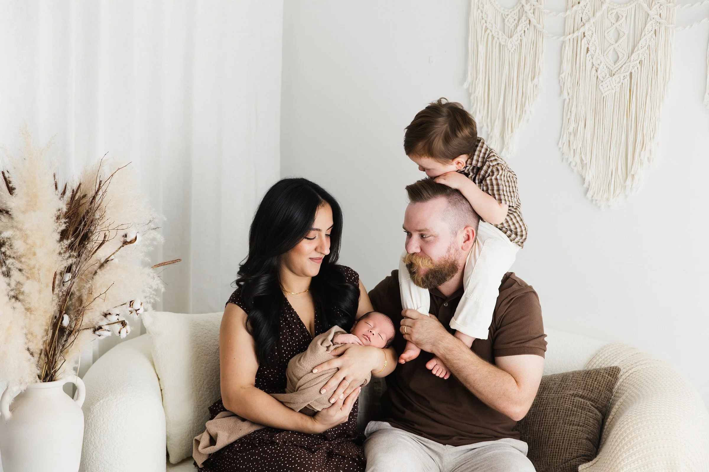 Parents gathered around their newborn while their older son sits on his father’s shoulders.