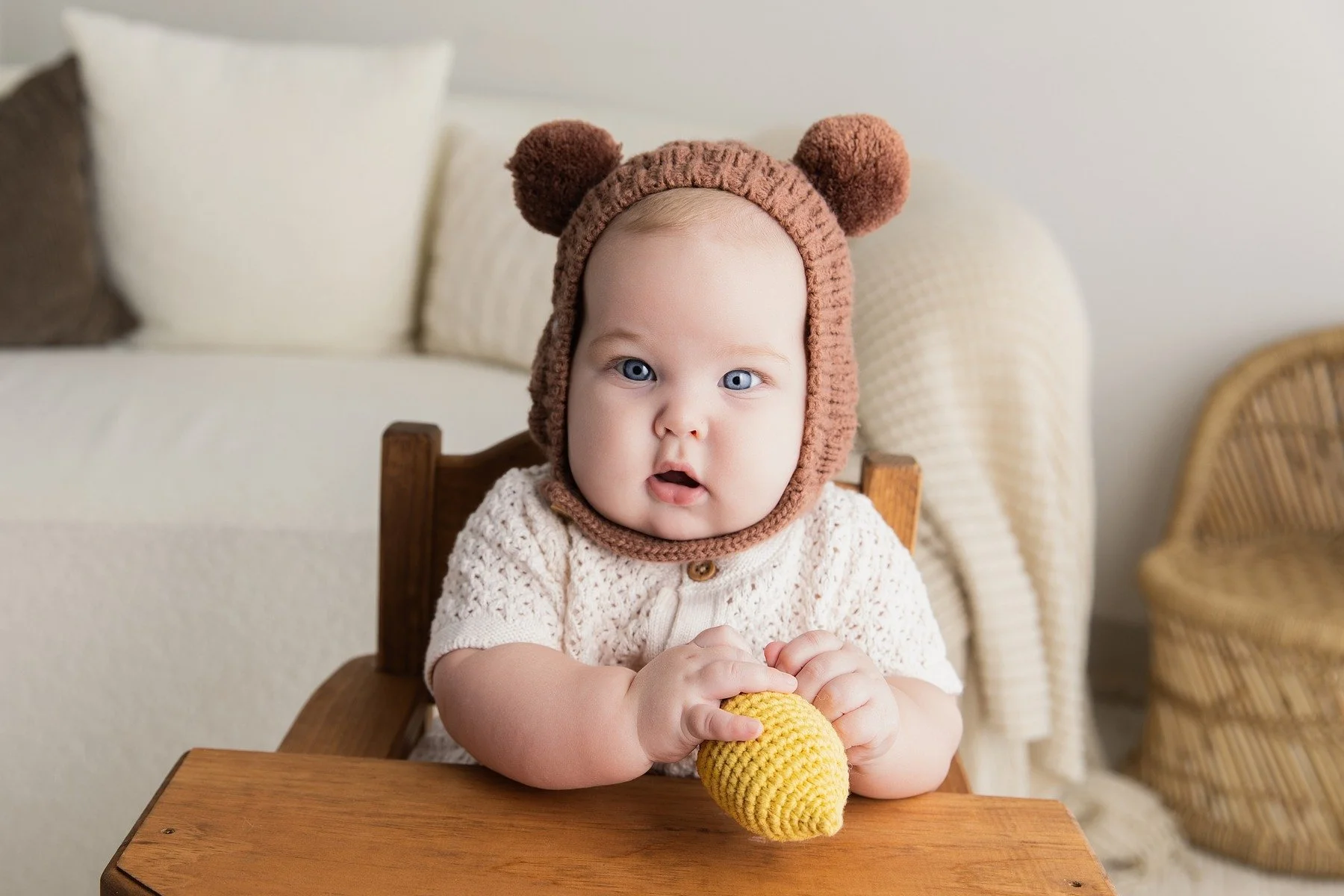 Six-month-old Paxton in a knitted bear bonnet holding a yellow toy