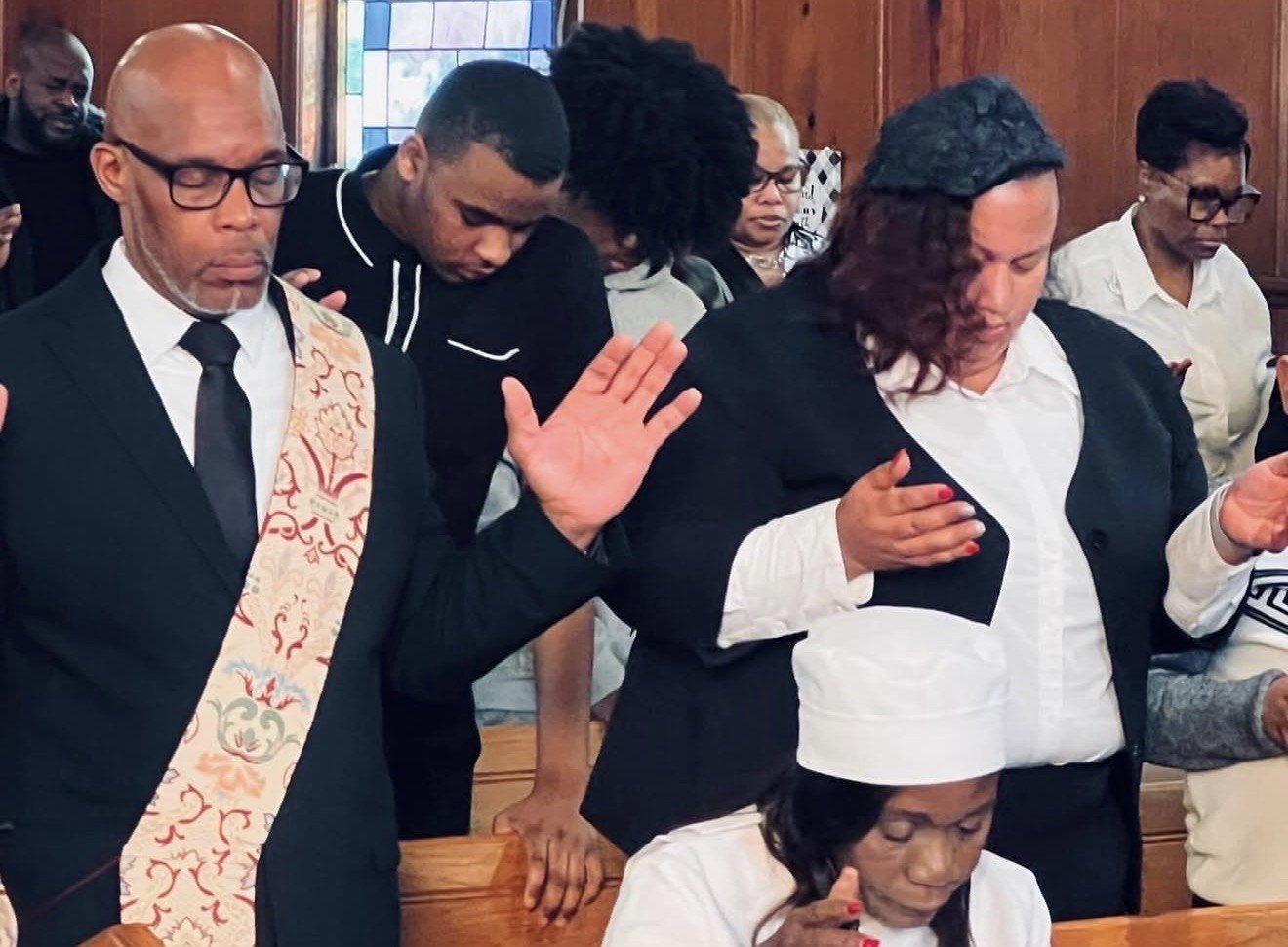 The LFT congregation stands together in prayer in the sanctuary, heads bowed and hands raised