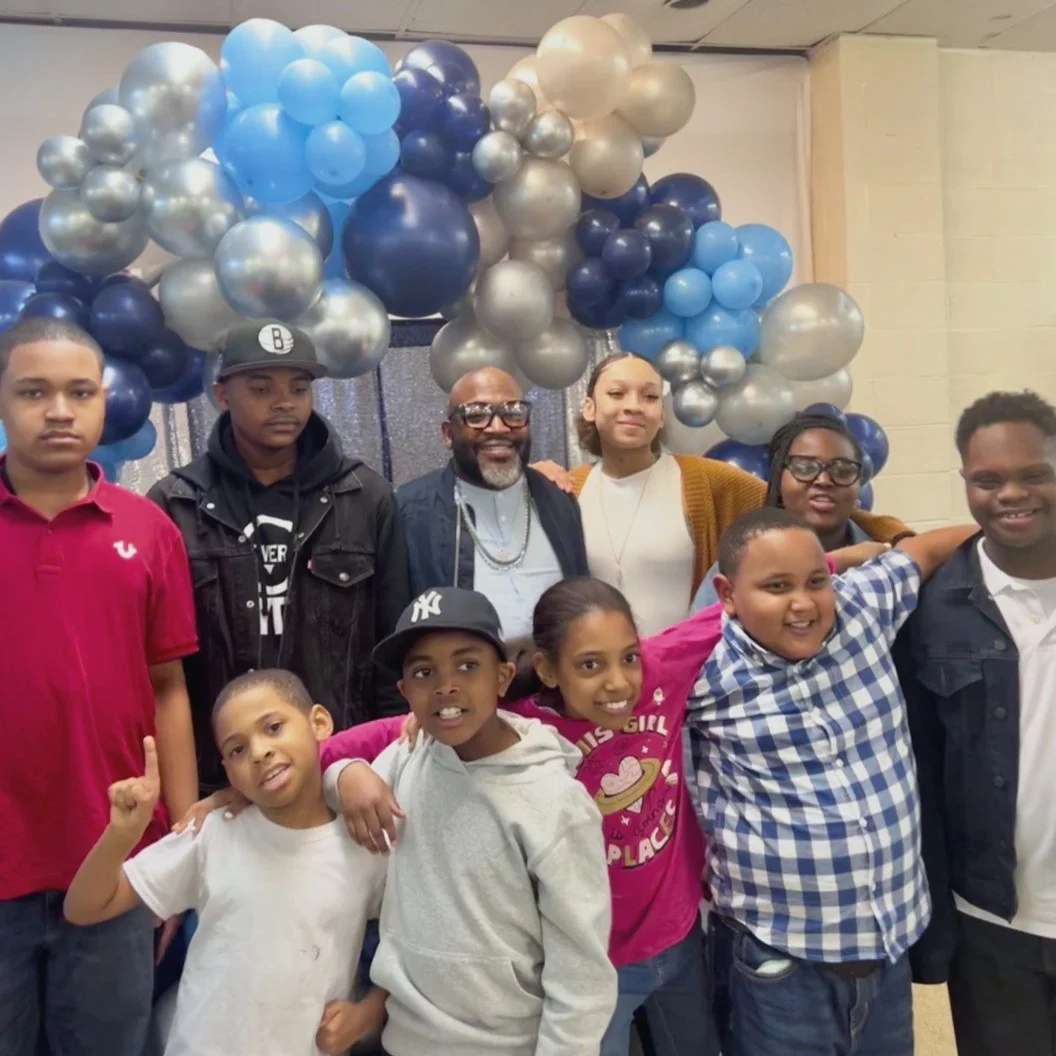 Bishop James H. Byrd with a group of LFT young people, smiling together in front of a blue and silver balloon arch