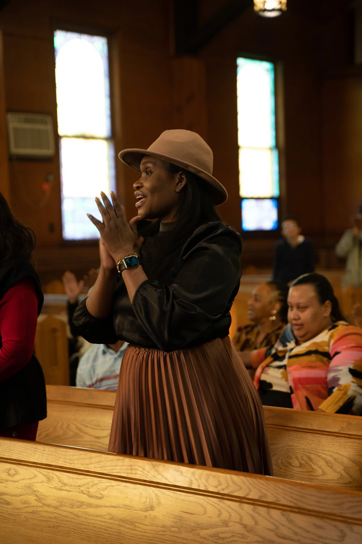 A woman in a tan hat worships with raised, clapping hands in the pews at LFT