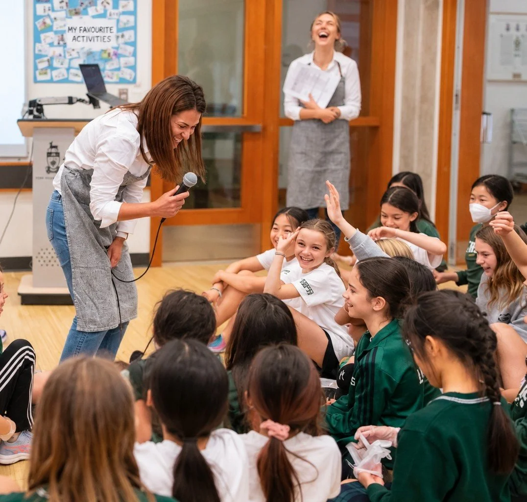 Students laughing and raising their hands during a nourishED Thrive workshop, seated together on the floor of a school gym