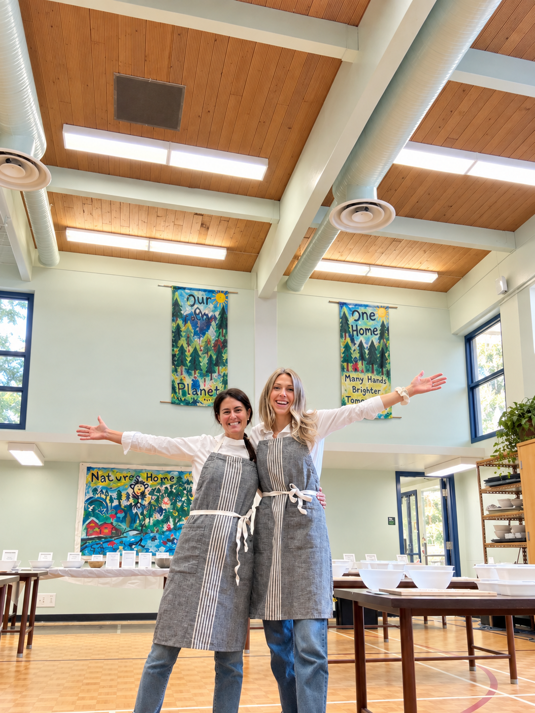 Emily and Golnaz standing together with their arms open, smiling, in a bright nourishED workshop space.