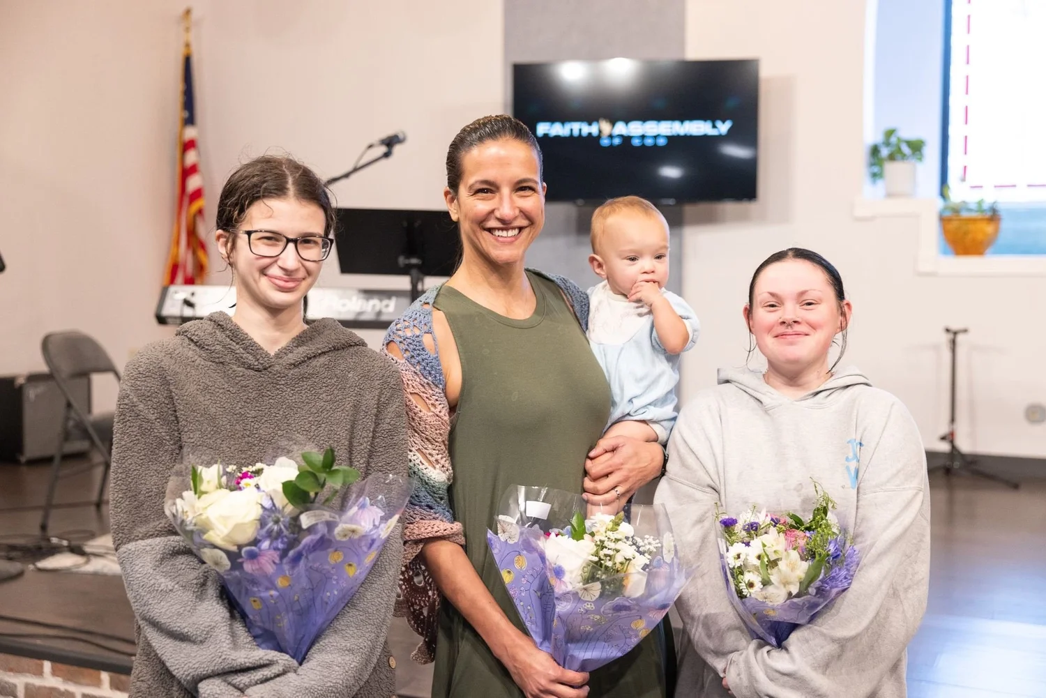 A mom, her baby, and two teens holding flowers