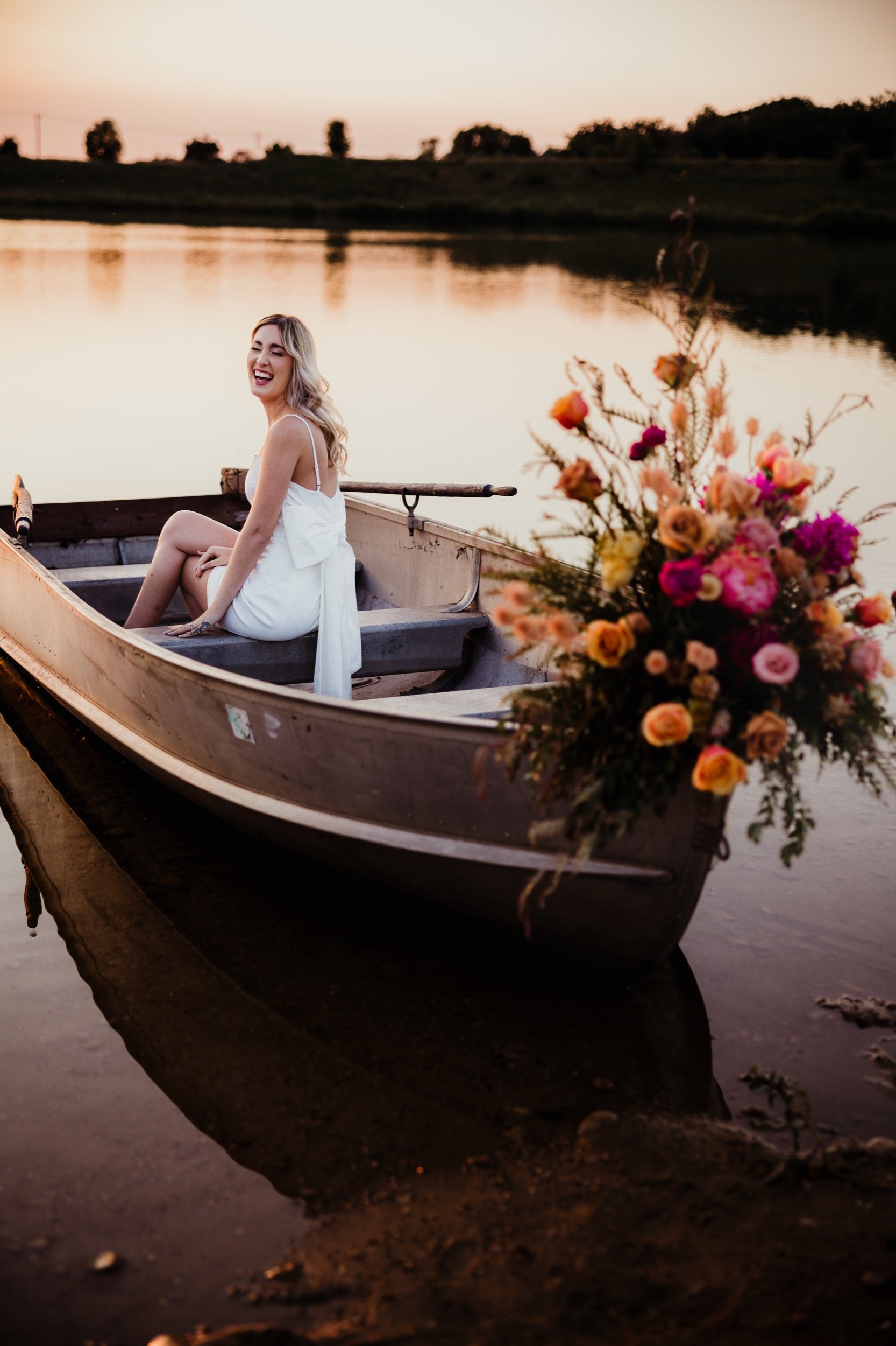 A woman laughing in a flower-filled boat at sunset
