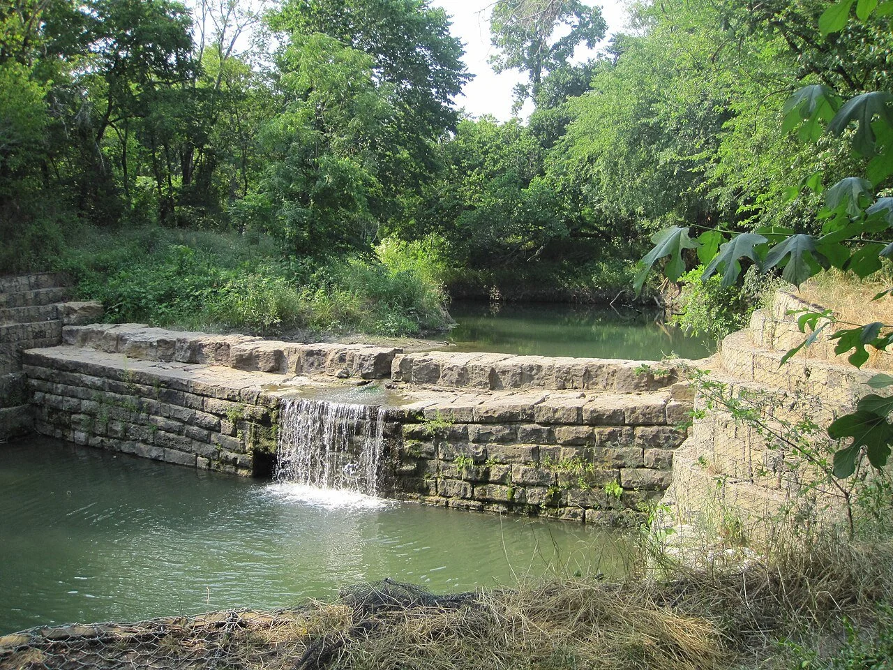 Water flowing over the historic stone dam at Allen Water Station, surrounded by green trees