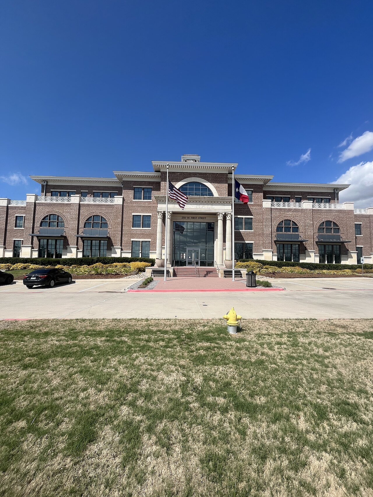Prosper Town Hall’s brick facade and flags under a blue sky