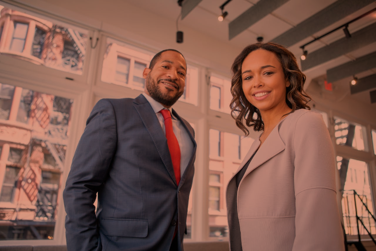 Two mid-aged executives (one male, one female) stand together smiling looking down towards the camera