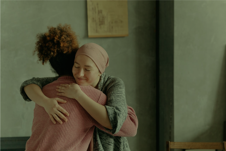 A female cancer patient is embraced by her female friend as they smile.