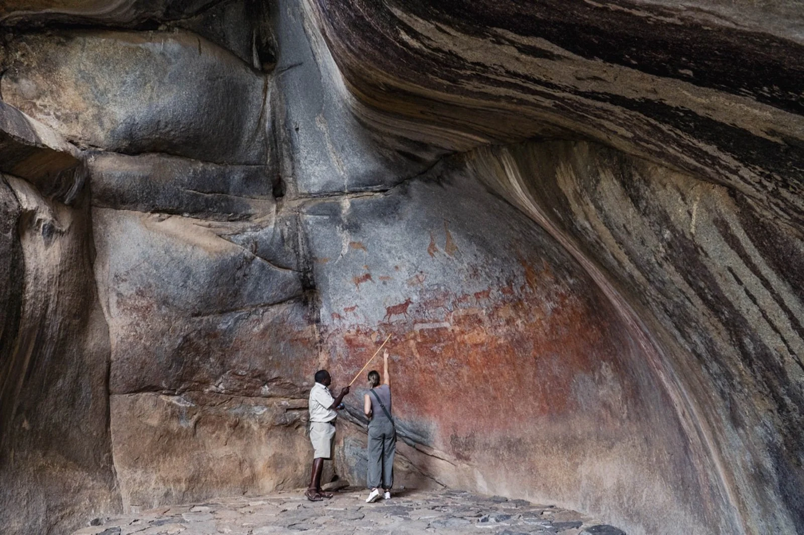 A guide and visitor looking at rock paintings beneath a granite overhang in Matopos