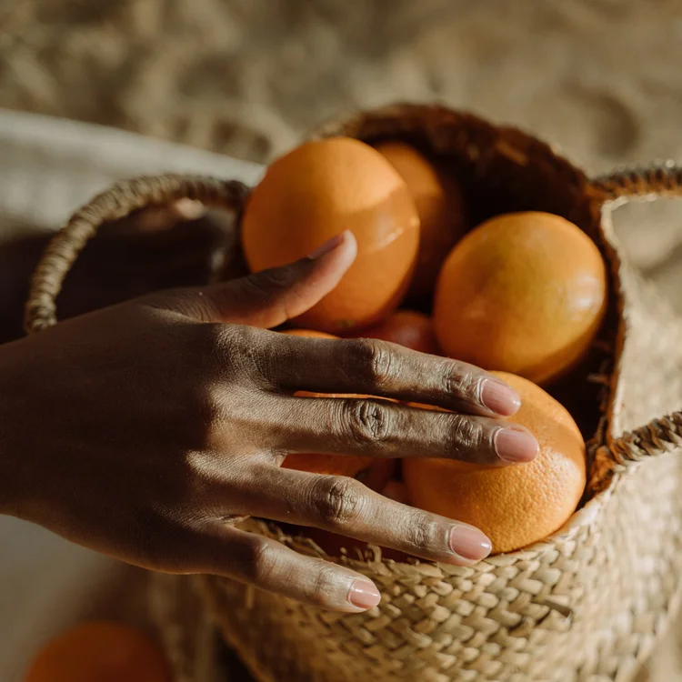A hand reaching into a basket of oranges