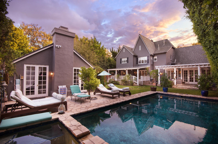 Gray shingled home with pool and loungers under a sunset sky