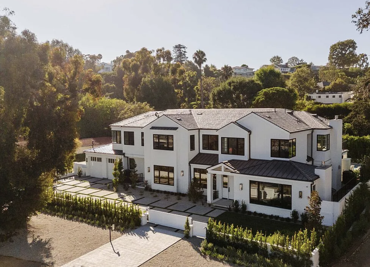 Aerial of a white traditional home with dark roof among trees