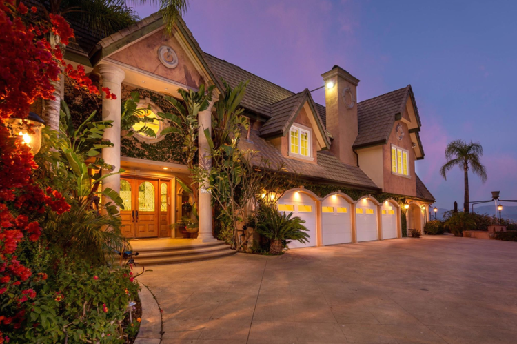 Columned stucco home with bougainvillea and three-car garage at dusk